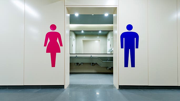 The doorway of a unisex bathroom, there is a large sticker of a lady one on the left side and man on the right. 
