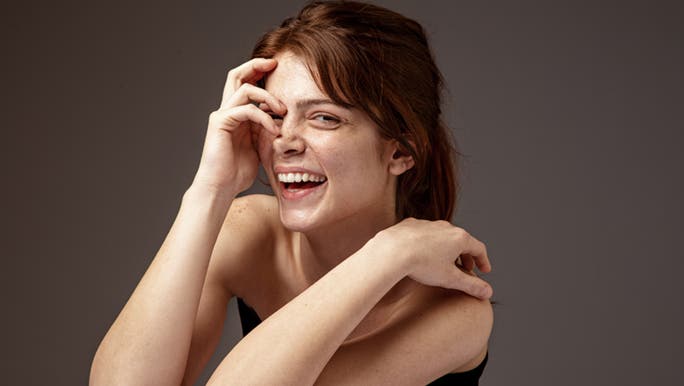 A happy woman laughs out loud while covering part of her face with her hand and wonders what skin number phototype she is. 