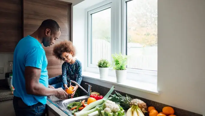 Dad and daughter washing vegetables at the kitchen sink