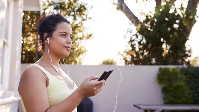 Young woman in yellow active wear listening to music on her smartphone getting ready to workout