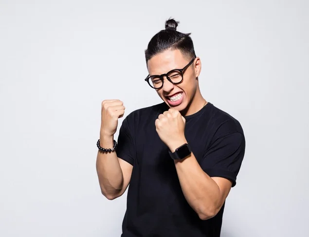 Happy young man in a black t-shirt and glasses clenching his fists