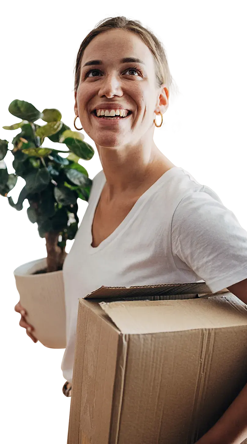 Woman looking upwards and smiling as she enters a room with a house plant and cardboard box.