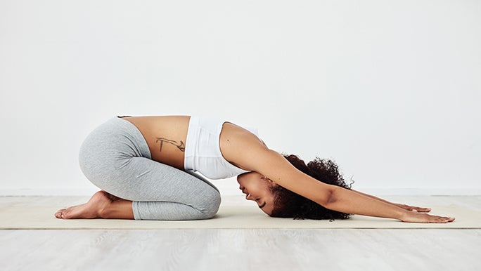 A woman is doing child’s pose, a yoga pose where you neel on the ground with your bum on your feet and fold forwards.