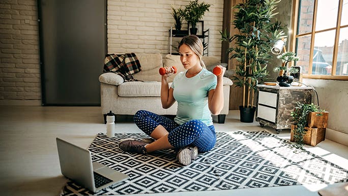 A woman works out at home in front of her laptop playing a group exercise video. 