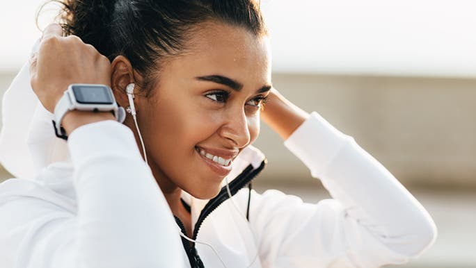 A woman is pulling up the hood on her jacket before exercise while wearing a fitness tracker in Australia.