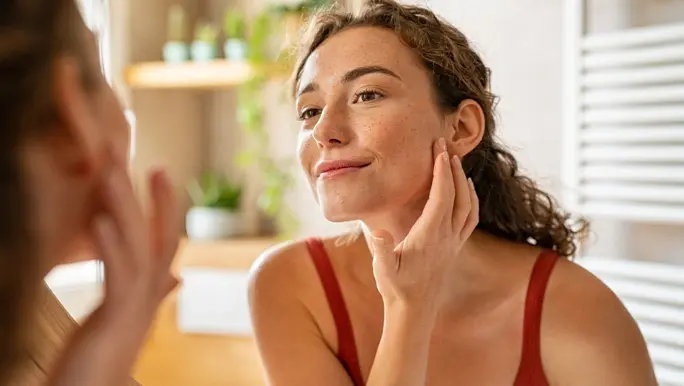 Woman with curly hair examining her skin type in the bathroom mirror
