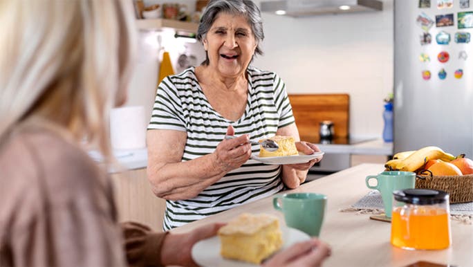 A senior woman is smiling and eating cake