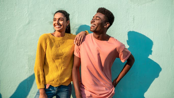 A couple in bright clothing are standing in front of a green rendered wall. They are currently enjoying the love language of quality time.