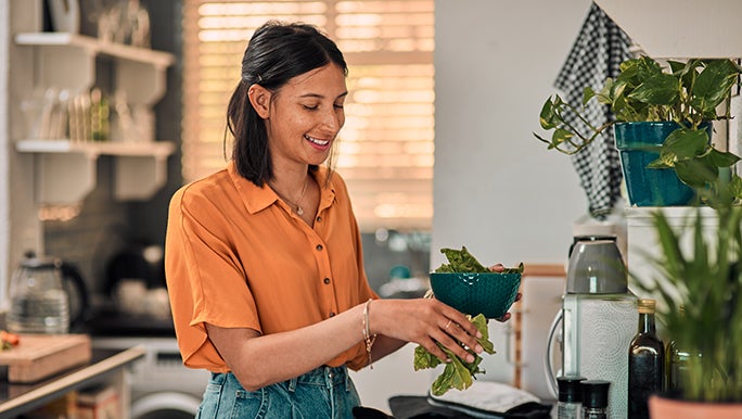 A smiling woman looks down on the piece of lettuce she is washing at the sink and knows that it’s not about ‘fixing’ gut health but finding what works for her.