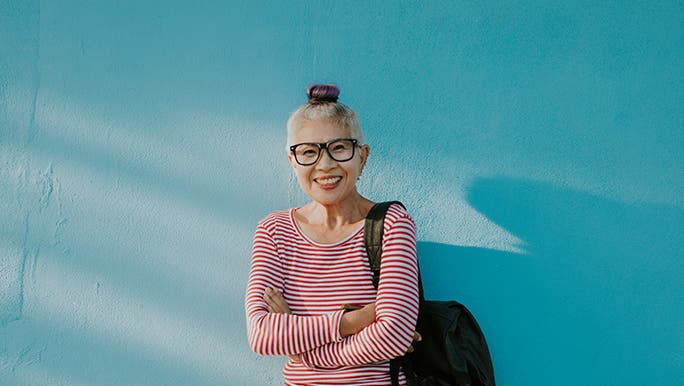 A woman stands in front of a blue wall smiling at the camera. 