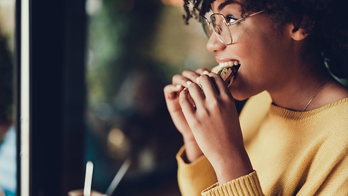 A woman is enjoying a piece of bread because improving gut health doesn’t mean you have to remove food such as bread.