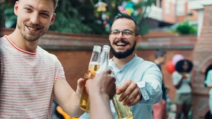 Two men are smiling while clinking beer bottles. 