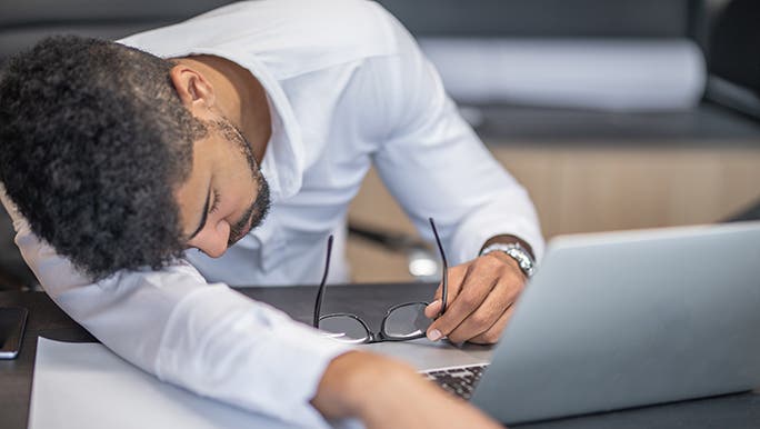 A business man puts his head on her arm and removes his glasses in front of a laptop while researching if you can catch up on sleep.
