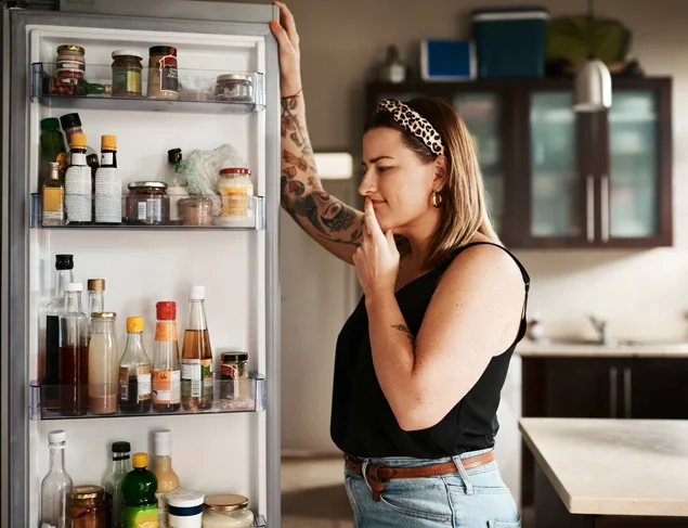 Woman in jeans and a black tank top looking in the fridge for something to eat