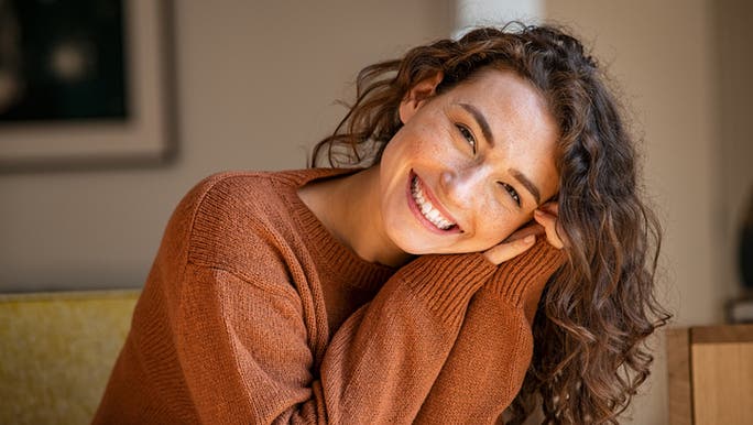 A young woman is smiling while holding her head in her hands