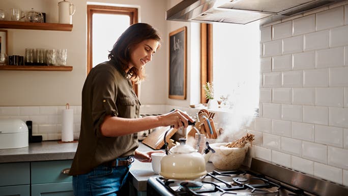 A woman is boiling a kettle on a gas stove, she is making tea in an attempt to keep her immune system healthy. 