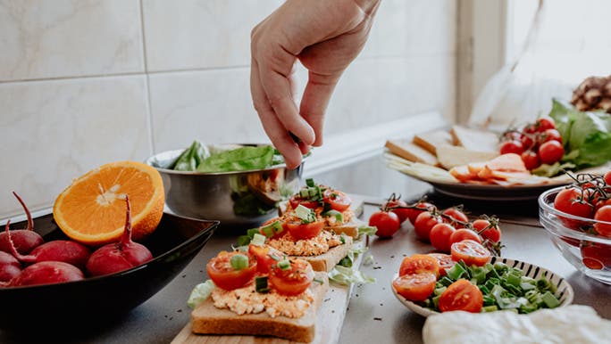 Someone sprinkles herbs over some healthy open sandwiches in a modern kitchen. 