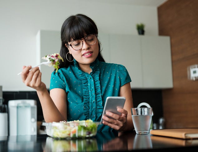 Young woman eating a salad and checking her phone