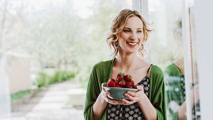 Healthy young woman in a green top eating strawberries