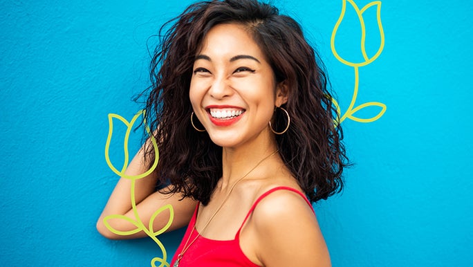 Happy young woman smiling in a red top in front of a blue wall