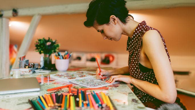 Young woman at her desk colouring in with bright coloured pencils