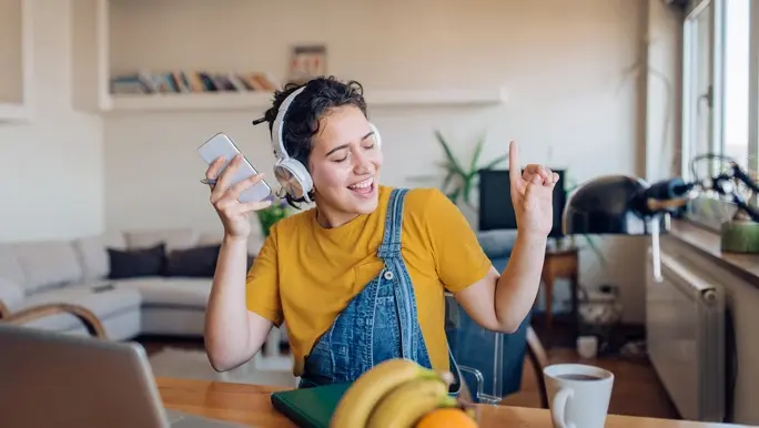 Relaxed young woman singing along to music she is listening too through headphones while working from home