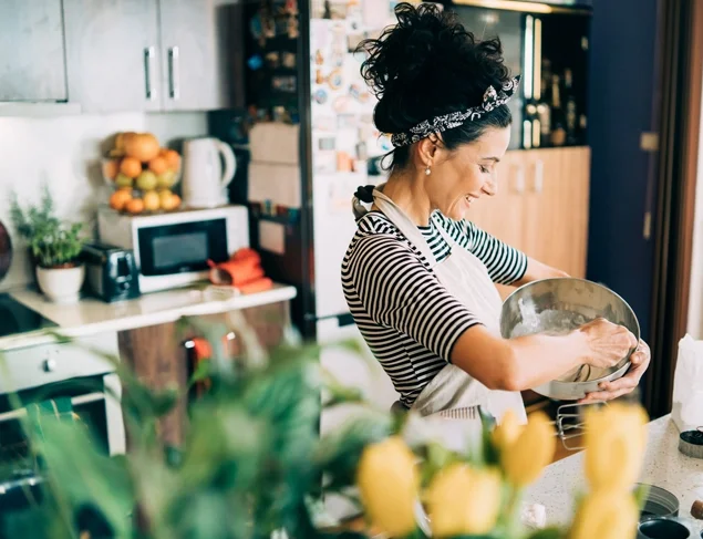 Happy woman in her kitchen wearing a black and white stripe top and apron making a calcium rich meal