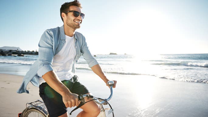 Smiling man enjoying the sun riding a bike at the beach