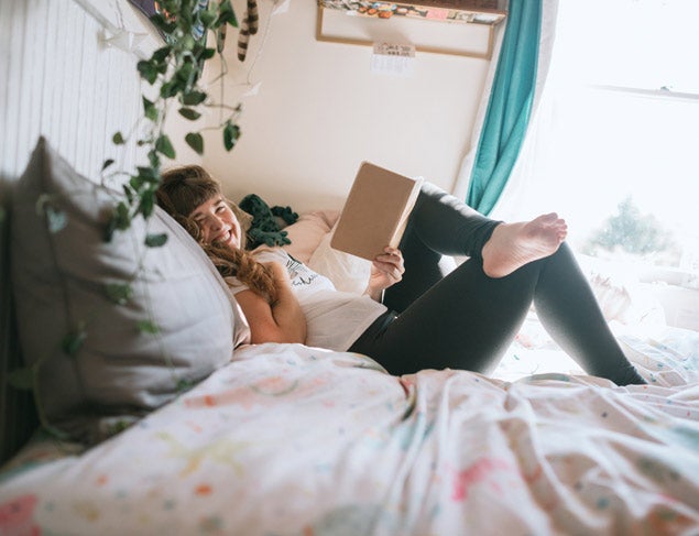 Happy young woman relaxing on her bed reading a book