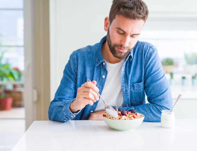 Man eating a healthy breakfast of muesli, berries and yogurt in his kitchen