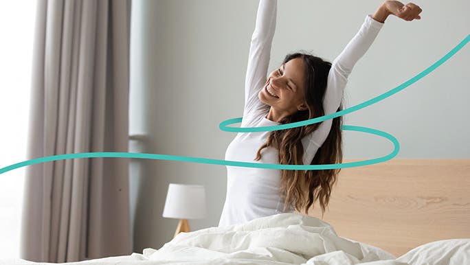 Young woman in white pyjama top sitting up and stretching in bed in the morning