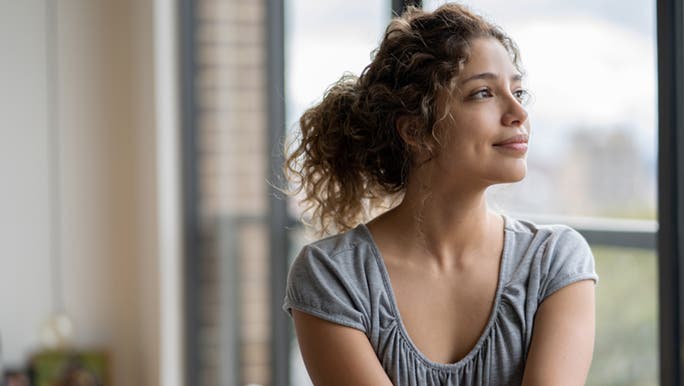 Looking calmly out her window, a woman finishes her positive affirmations to help with mild anxiety.
