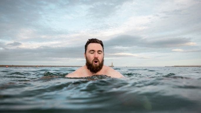 A young Caucasian man is taking a cold shower and flinching at the temperature