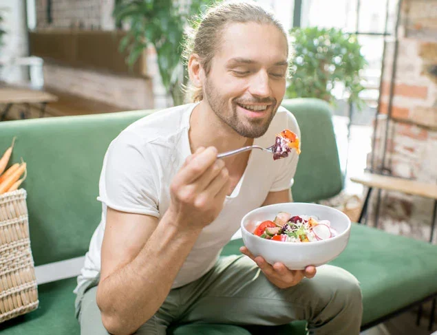 Young man sitting on a green couch eating a healthy fermented vegetable salad