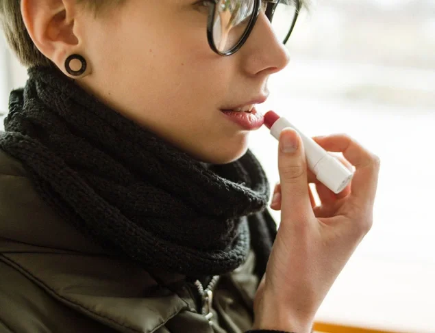Woman with short blonde hair and glasses applying lip balm