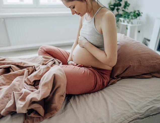 Pregnant woman sitting up in bed cradling her belly