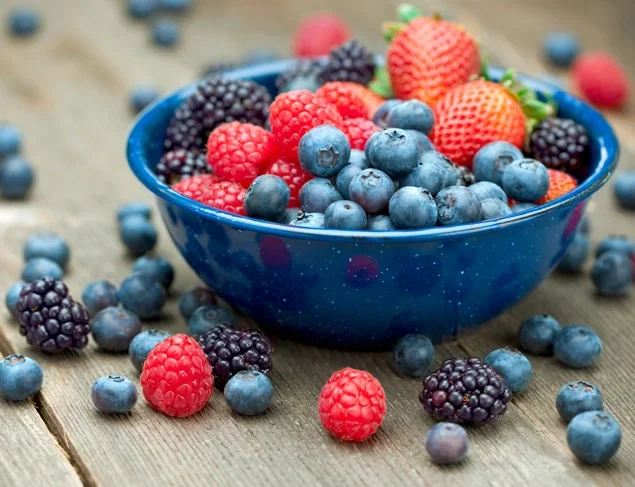 Low FODMAP raspberries, blueberries and blackberries in a blue bowl on a timber surface