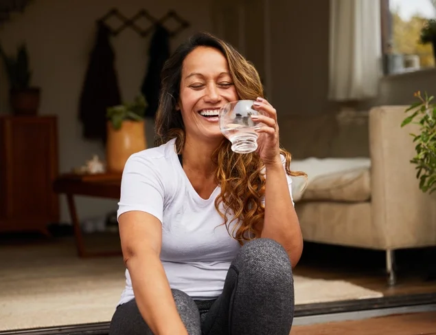 Woman laughing in active wear drinking a glass of water