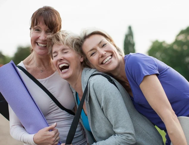 Three female friends laughing after an outdoor yoga class