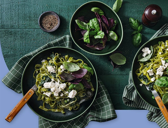Two bowls of spinach and feta pasta with a green side salad