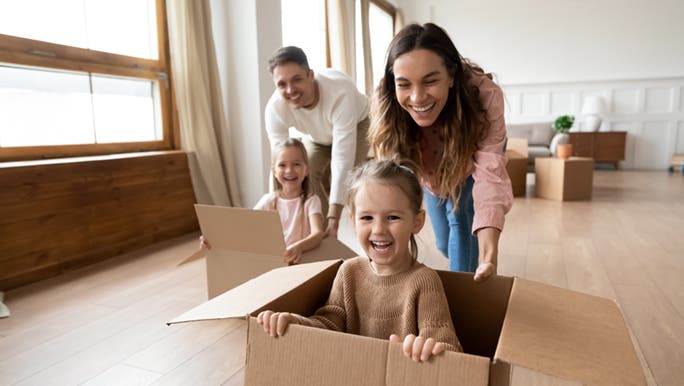Two parents are pushing their kids around in empty cardboard boxes. Everyone looks happy. 