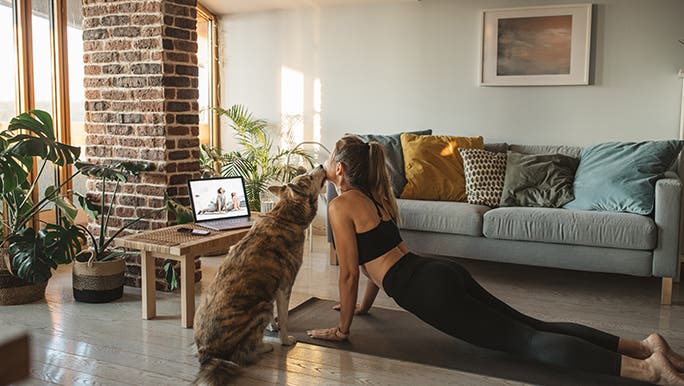 A woman practices Yoga in her lounge room with her dog. She is using self-care to combat brain fog. 