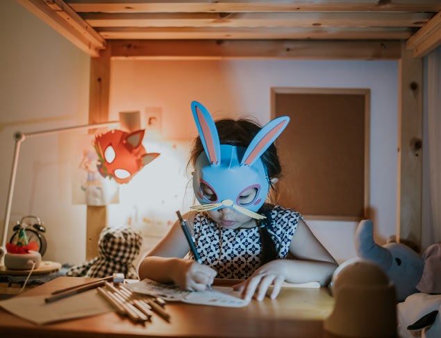 Young girl wearing a rabbit mask doing her homework