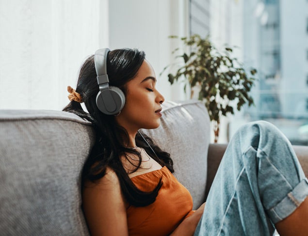 Young woman using headphones while relaxing on the lounge at home