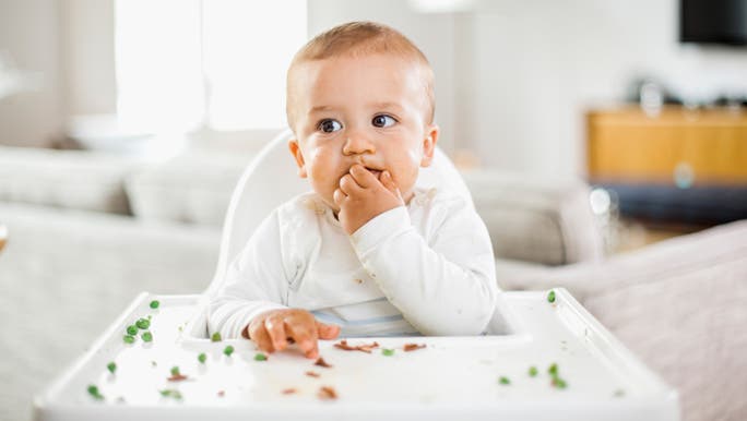 Baby boy in his high chair eating green peas