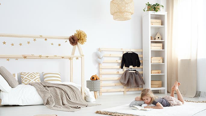 A child is lying on the floor reading a book in a beautifully minimalist bedroom  as her parents bought good quality unisex products. 