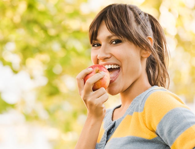 Smiling young woman eating a red apple in the park