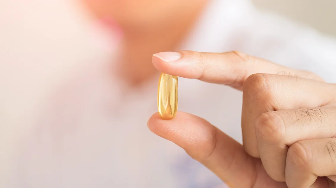 Woman holding am oil capsule supplement in between her thumb and forefinger
