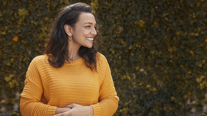 A happy woman is holding her hands near her stomach as though she has good gut health.