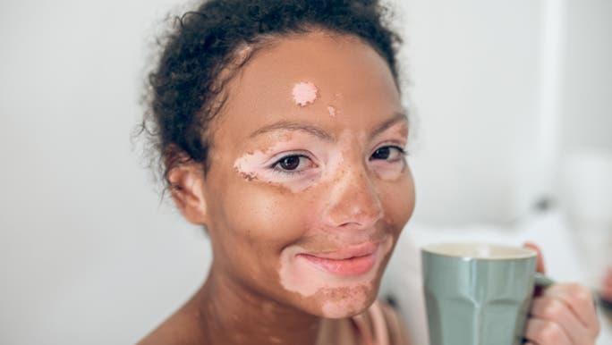 A woman smiles and drinks coffee while reading about how to find out what skin type she is.
